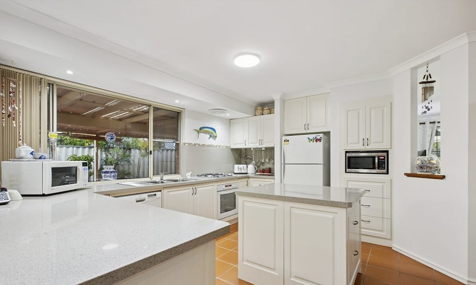 The kitchen, with an island bench, stone tops and a servery window through to the patio.
