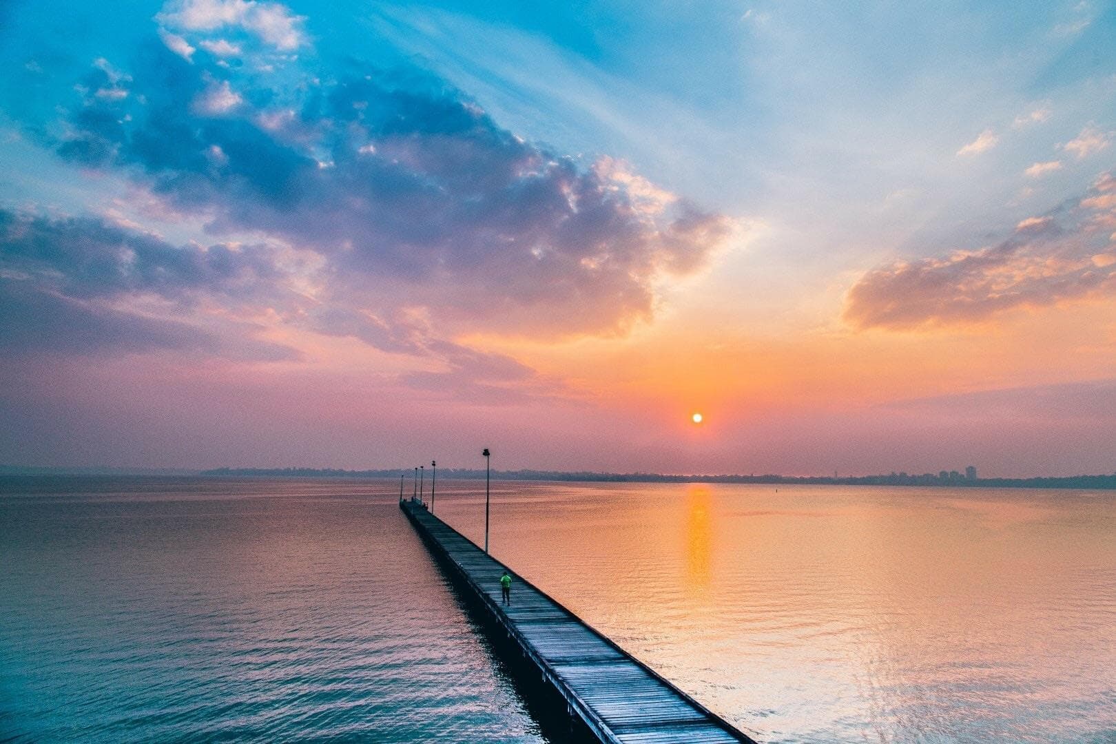 The Como jetty reaching into the Swan River at sunset, with a single figure walking along it.