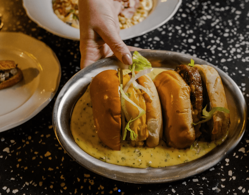 Cheeseburgers on a metal tray with a herb sauce, being served at a restaurant table.